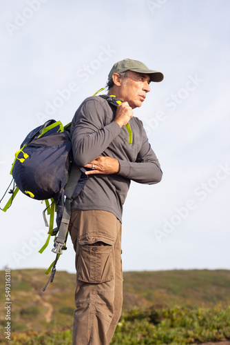 Portrait of concentrated elderly man with backpack. Sporty man in casual clothes during hike on summer day. Sport, adventure, hobby concept