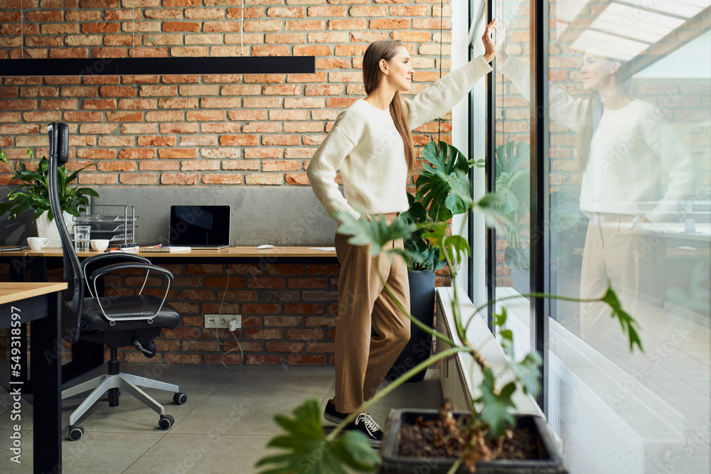 Thoughtful  female entrepreneur looking through window in small startup office