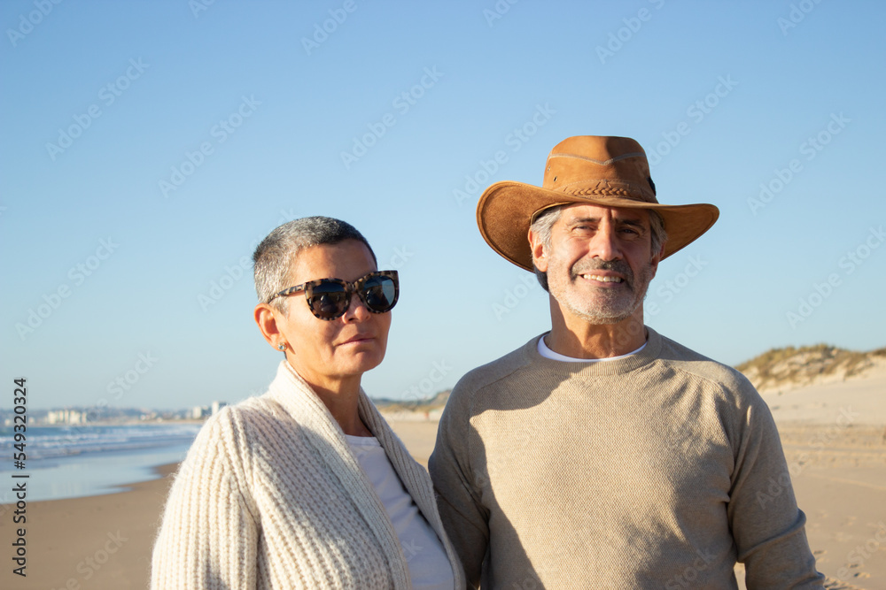 Portrait of lovely senior couple at seashore. Handsome grey-haired man in cowboy hat and short-haired woman in sunglasses spending vacation at seaside. Retirement, leisure concept