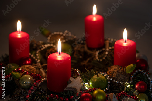 Advent and Christmas lights, four red candles on a wreath with decoration against a dark background, copy space, selected focus