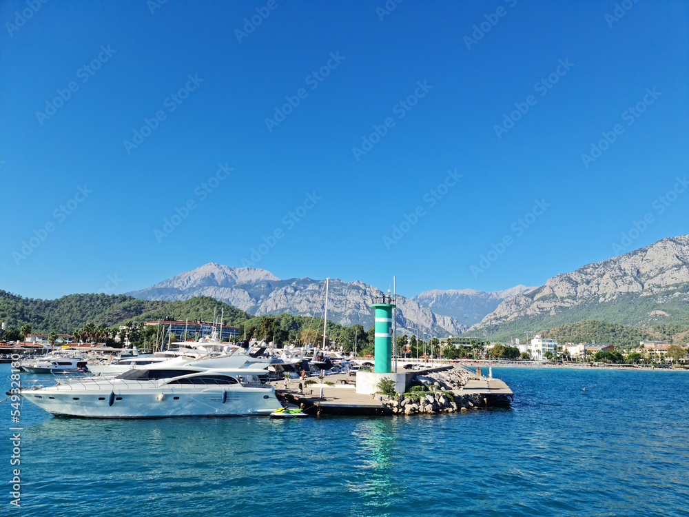 22 Oct 2022 a boat trip in Kemer, Antalya, Turkey. Port with blue sea, private boats, small greenish lighthouse and a wonderful mountains behind it, blue sky, sunny.