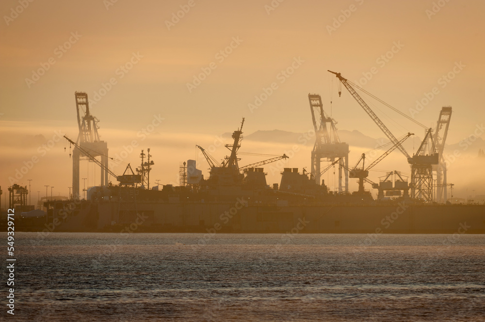 Cranes and Dry Dock Lifts in Elliott Bay, Seattle, Washington During a Beautiful Sunrise. Industrial shipping and heavy equipment are silhouetted on a foggy morning in the Pacific Northwest. 
