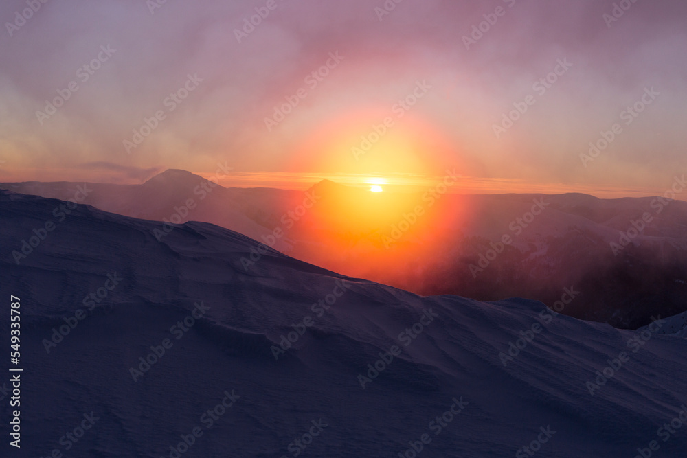 Bright orange sunrise of the sun disk in the snowy mountains