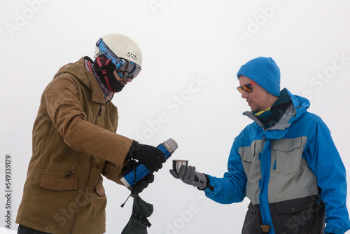 Two hikers in the winter mountains are sharing warm tea from a thermos