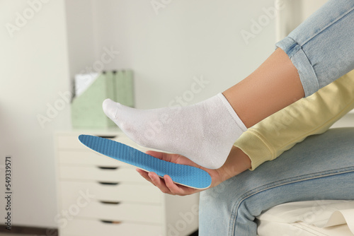 Woman fitting orthopedic insole to her foot indoors, closeup