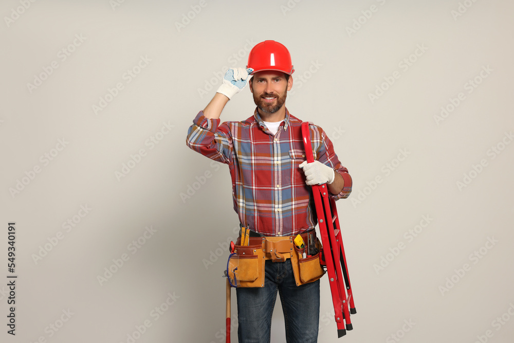 Professional builder in hard hat with tool belt and step ladder on light background Professional builder in hard hat with tool belt and step ladder on light background