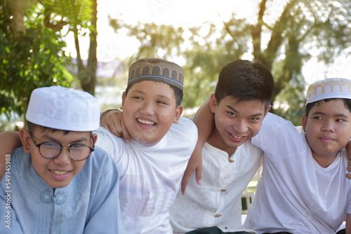 Young asian Muslim boys are playing with their hands behind each other by sitting in a row happily under a tree in the school park, soft and selective focus. © Sophon_Nawit