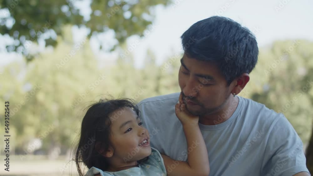 Happy little daughter kissing father on cheek, man taking photo with camera. Young Asian man sitting with toddler girl in park. Fatherhood and childhood concept Happy little daughter kissing father on cheek, man taking photo with camera. Young Asian man sitting with toddler girl in park. Fatherhood and childhood concept