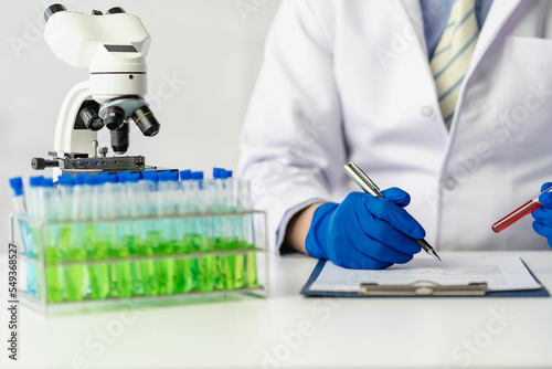 Doctor taking test tube with blue liquid, virologist working in chemical protective suit man studying dangerous virus Biologist at the lab table with a microscope in the laboratory