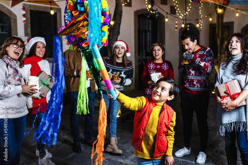 Hispanic child boy with Mexican family breaking a pinata at traditional posada party for Christmas in Mexico Latin America photo