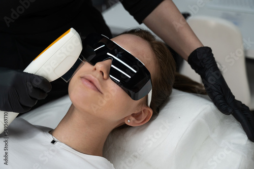 Young caucasian woman in goggles on photorejuvenation procedure. Portrait of a girl in a beautician's clinic.