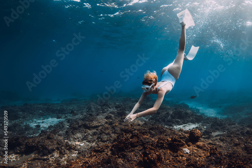 Woman freediver in white swim wear dive with fins over corals. Freediving in tropical blue ocean