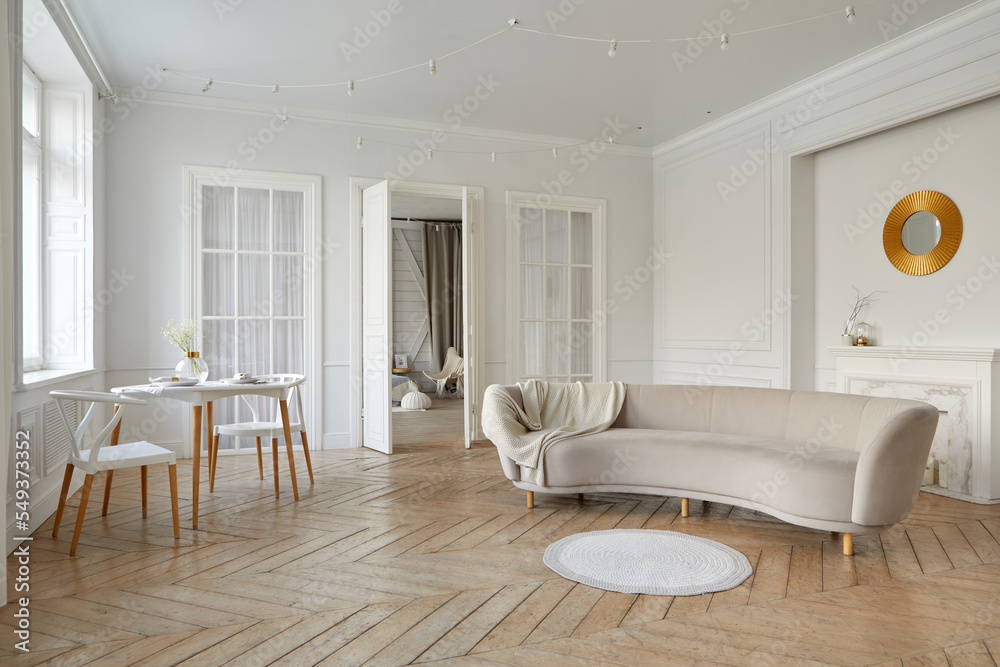 Fototapeta premium Interior of light lounge with white walls and solid herringbone oak parquet with round table decorative lights on ceiling and oval beige sofa