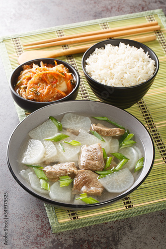 Korean Beef Radish Soup Sogogi Muguk served with rice and kimchi closeup on the mat on the table. Vertical