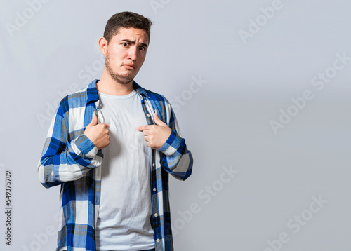 Confused caucasian young man pointing at himself. Confused person pointing at himself isolated. Confused latin guy pointing at himself isolated, Portrait of confused teenager pointing at himself photo