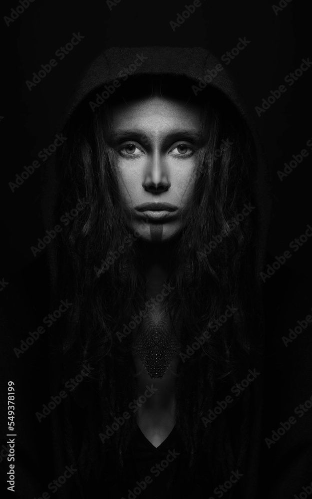Fine art and sci-fi concept. Abstract and futuristic looking alien or extraterrestrial close-up portrait. Model with long hair hiding under hood and staring at camera. Black and white image