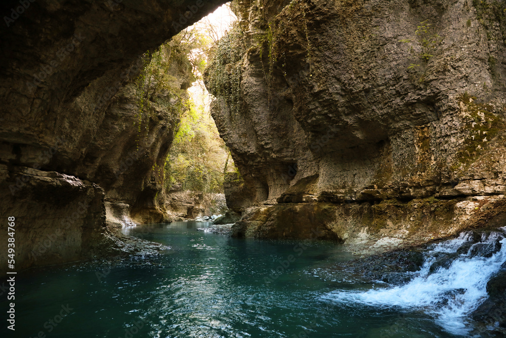 Picturesque view of clean river near cliffs and waterfall outdoors Picturesque view of clean river near cliffs and waterfall outdoors