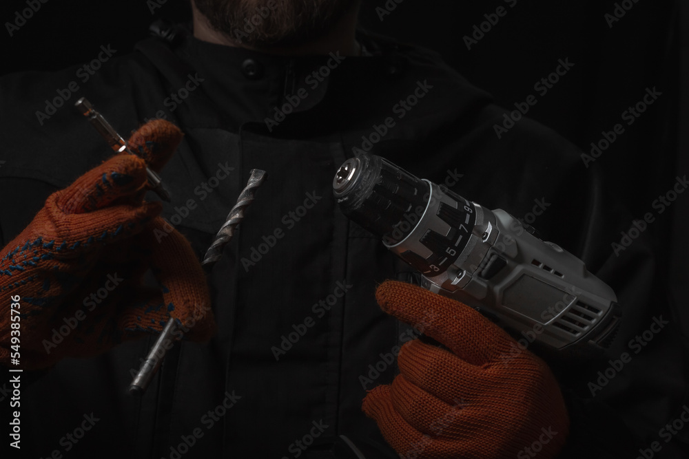 Hand holds cordless electric screwdriver with bit for screws and drilling isolated on black background