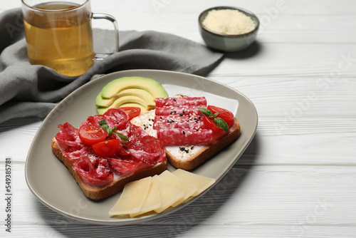 Tasty toasts with slices of sausages, tomatoes and cheese on white wooden table