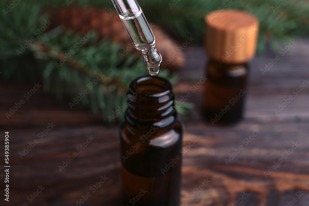 Dripping pine essential oil into bottle at wooden table, closeup