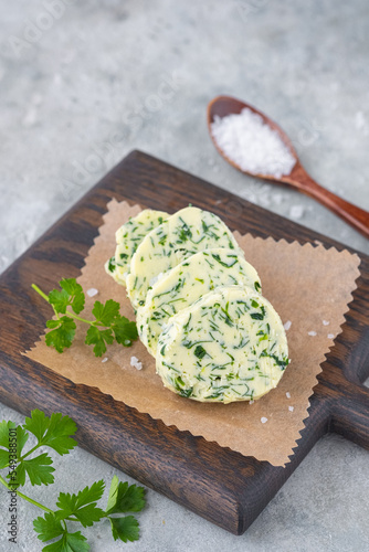 Butter with parsley and salt, cut into circles, on a brown wooden board on a gray concrete background. Types of butter for serving dishes.