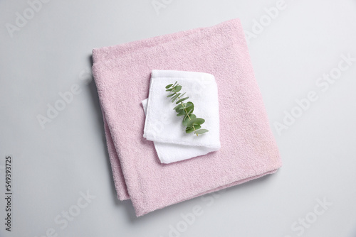 Soft folded towels with eucalyptus branch on light grey background, top view