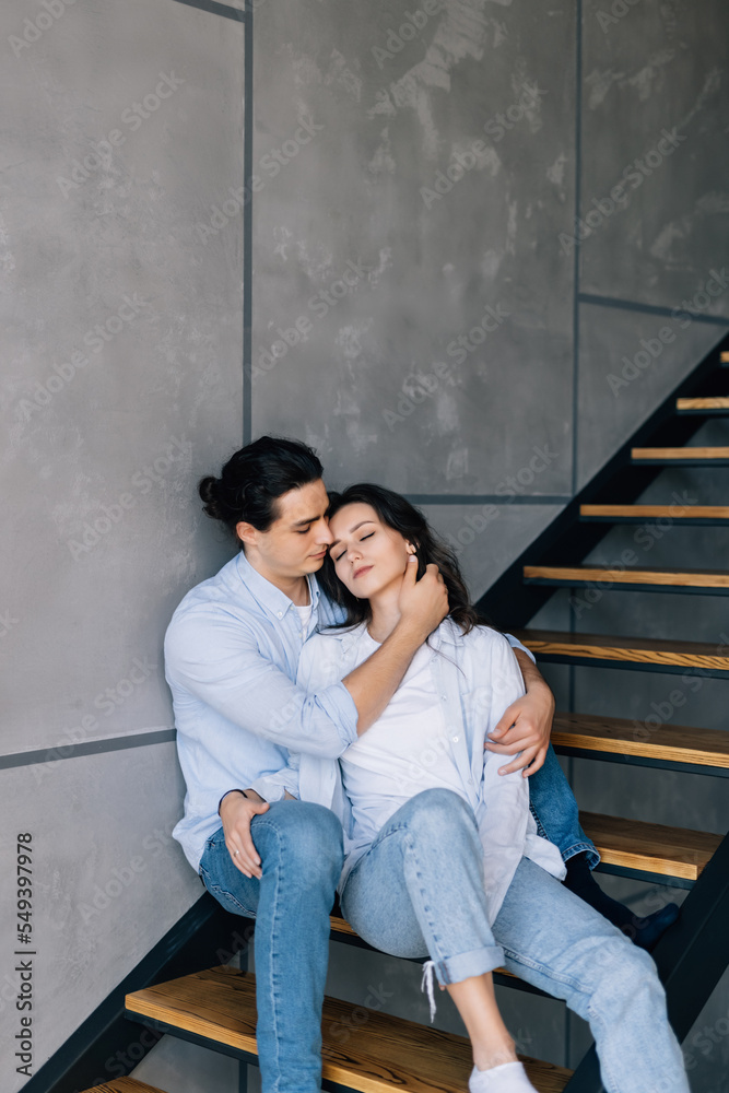 Naklejka premium A young couple in love is sitting on the stairs of their house