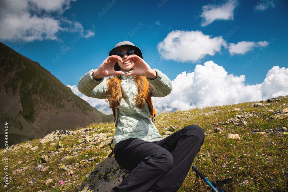 smiling young woman showing fingers gesture sign of heart, love in mountains, happy tourist