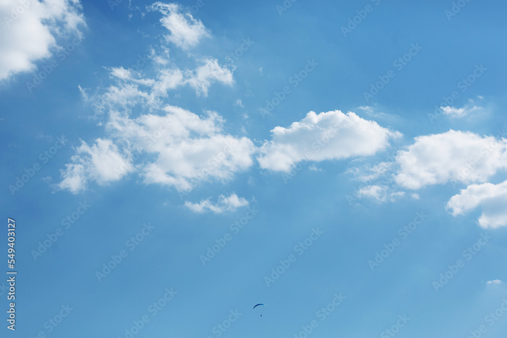 Blue Paraglider flying into the sky with clouds on a sunny day