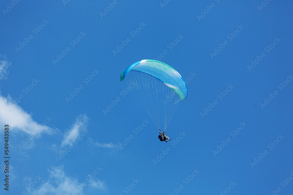 Blue Paraglider flying into the sky with clouds on a sunny day Blue Paraglider flying into the sky with clouds on a sunny day