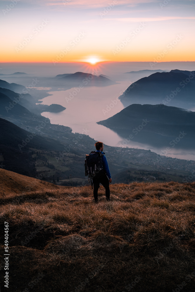 A hiker is walking on top of Punta Almana at sunset, with the Iseo Lake in the background, Northern Italy