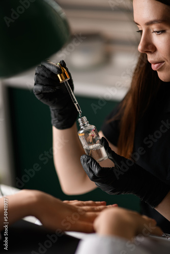 Selective focus on cosmetic bottle with pipette in hands of woman beautician.