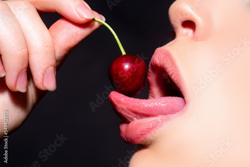 Cherry in woman mouth. Cherries on woman lips. Tongue lick cherry, macro, close up. Sexy tongue. photo