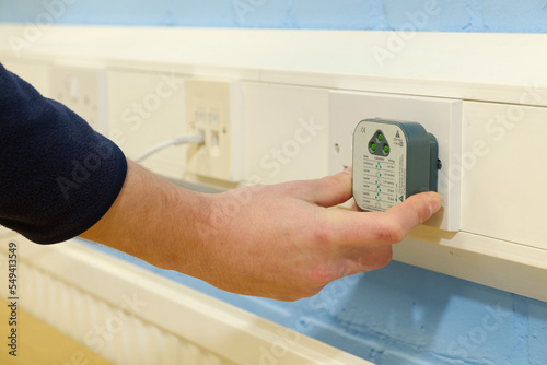 Close-up of electrician's hands using electrical circuit tester on UK double wall socket in office