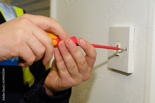 Close-up of electrician tightening fixing screw on UK light switch in office