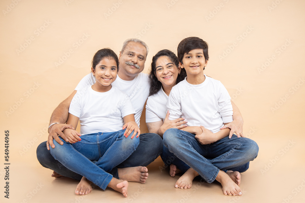 Happy indian grandparents with kids wearing white casual t-shirt sitting together over isolated beige background. Happy indian grandparents with kids wearing white casual t-shirt sitting together over isolated beige background.