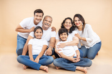  Portrait happy indian asian multi generation family wear white t-shirt sitting against beige background, mom,  dad, grandma, grandpa, two little kids together.