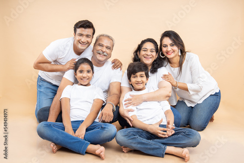 Fotografie Portrait happy indian asian multi generation family wear white t-shirt sitting against beige background, mom,  dad, grandma, grandpa, two little kids together