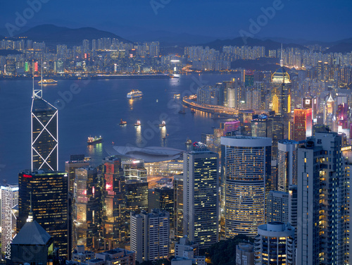 Blue hour landscape of Hong Kong Harbour and Kowloon  showing neon-lit skyscrapers  ships and boats.