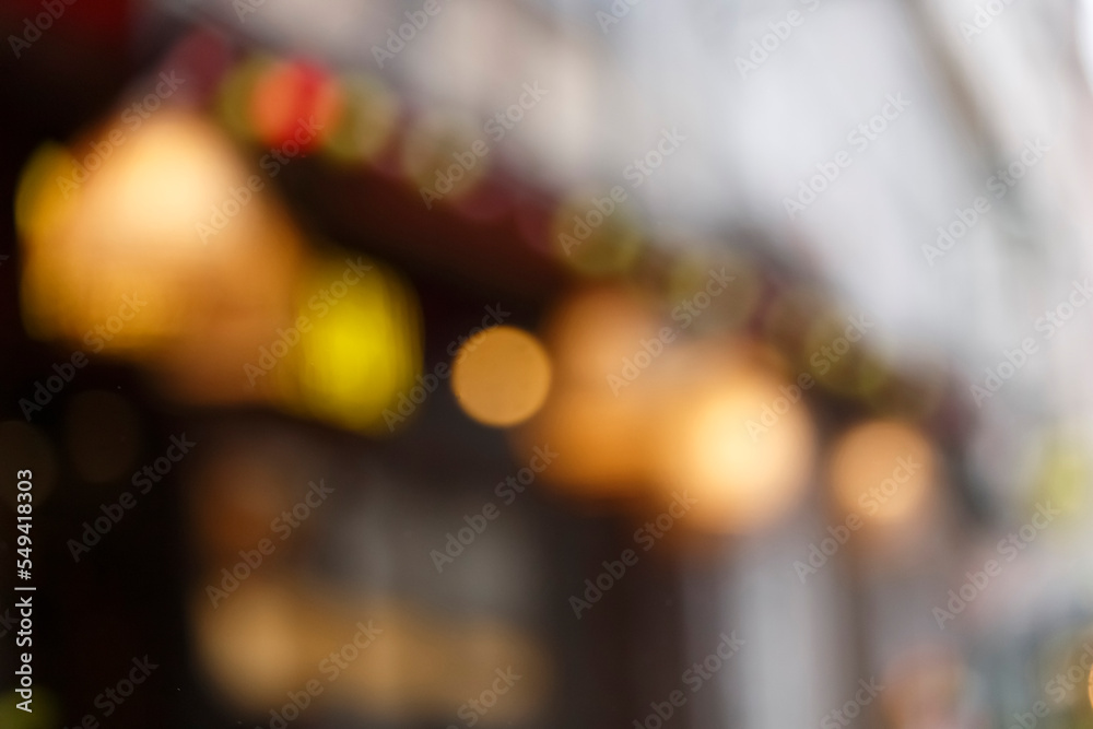 Blur background of European city street with bokeh of garlands, shop windows, cafe signboards