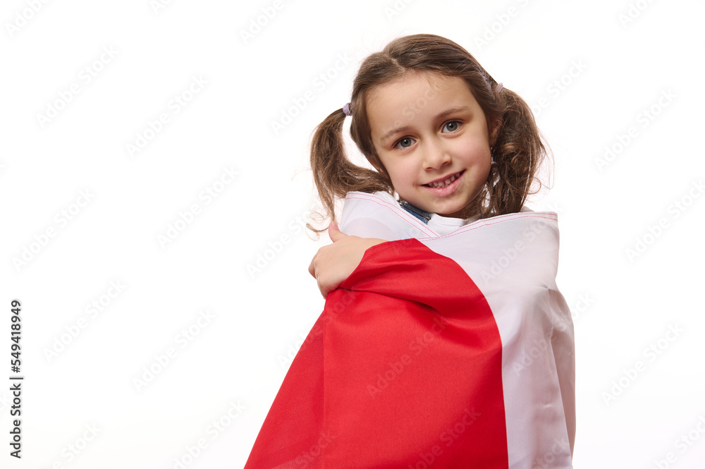 Isolated portrait on white background of a beautiful little child girl, proudly wrapping in flag of Poland or Canada. Concept of national holidays and patriotic events. Patriotism. Independence Day Isolated portrait on white background of a beautiful little child girl, proudly wrapping in flag of Poland or Canada. Concept of national holidays and patriotic events. Patriotism. Independence Day