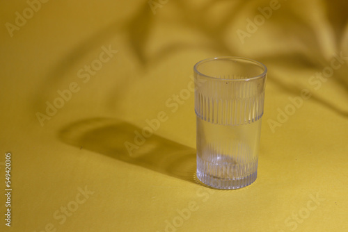 Fotografie A glass kept on a yellow background with the shadow of a plant