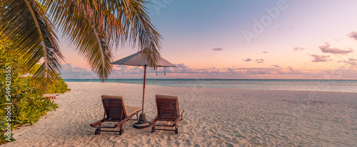 Amazing sunset beach. Romantic couple chairs umbrella. Tranquil togetherness love concept scenery, relax beach, beautiful landscape design. Getaway tropical island shore, palm leaves, idyllic sea view