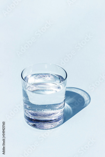 A blue glass of water with sharp strong shadow on blue background with copy space