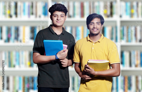 Young indian college or school boys holding books in hand standing in library.