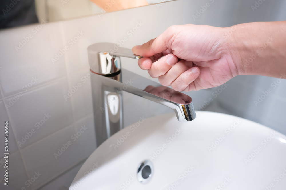 Male hand closing water tap or faucet in bathroom. Save water at home or water conservation