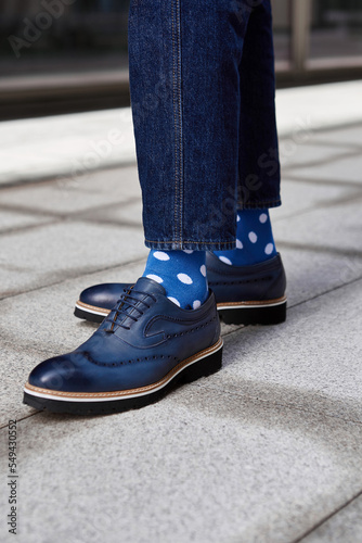 Legs of a man in blue jeans, dotted socks and elegant shoes on the street