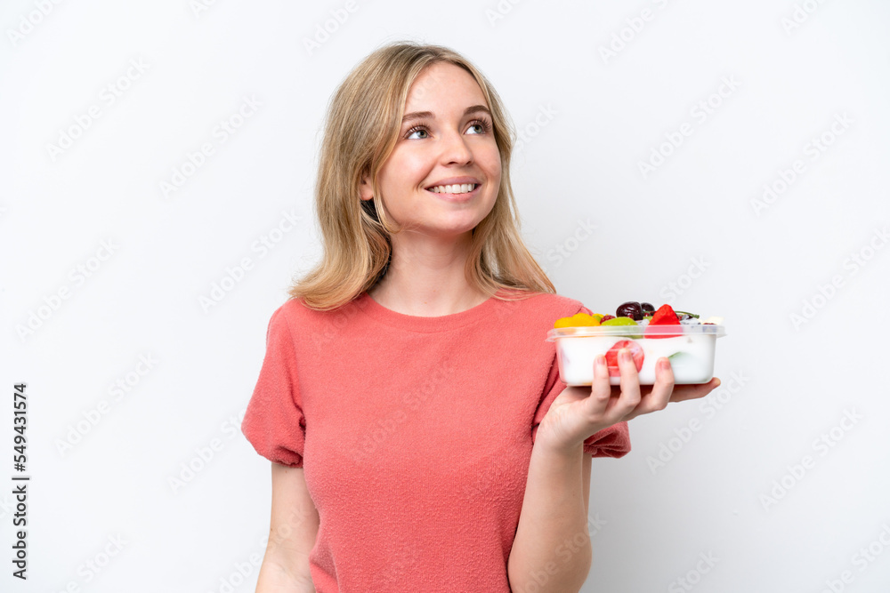 Young English woman holding a bowl of fruit over isolated white background looking up while smiling Young English woman holding a bowl of fruit over isolated white background looking up while smiling