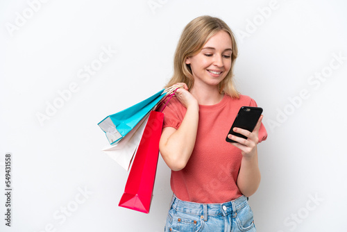Young English woman isolated on white background holding shopping bags and writing a message with her cell phone to a friend