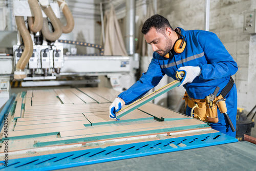 Handsome carpenter man in blue uniform use tape measure with machine at wood factory 